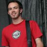 Dedi Herde in rotem T-Shirt mit Gitarrengurt, lächelt in die Kamera